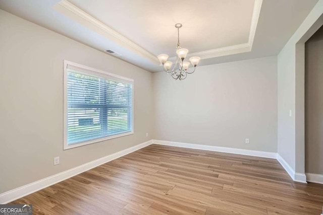 empty room featuring an inviting chandelier, a tray ceiling, and hardwood / wood-style floors