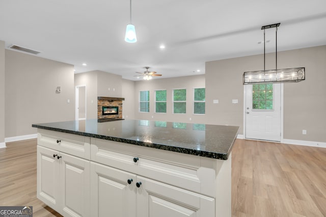 kitchen with ceiling fan with notable chandelier, plenty of natural light, light hardwood / wood-style flooring, and a stone fireplace