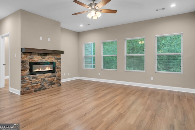 unfurnished living room with light hardwood / wood-style floors, ceiling fan, and a stone fireplace