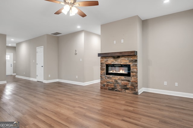 unfurnished living room with ceiling fan, hardwood / wood-style floors, and a stone fireplace