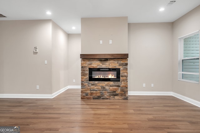 unfurnished living room featuring wood-type flooring and a stone fireplace