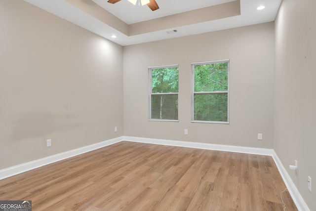 spare room featuring light hardwood / wood-style floors, a tray ceiling, and ceiling fan