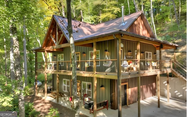 back of house with board and batten siding, metal roof, and a patio