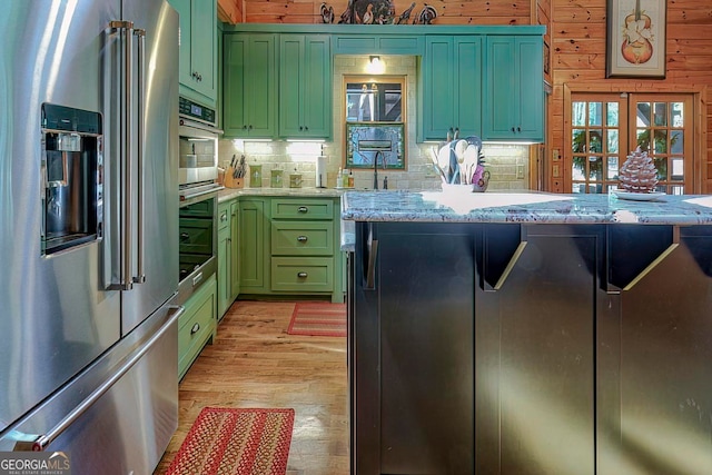 kitchen featuring decorative backsplash, green cabinets, wooden walls, high end refrigerator, and light wood-type flooring