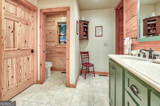 bathroom featuring wood walls, vanity, tile patterned floors, and toilet