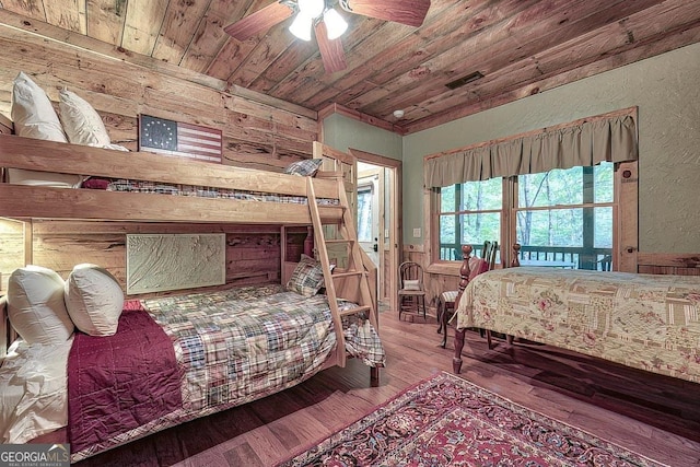 bedroom featuring visible vents, a textured wall, wooden ceiling, hardwood / wood-style floors, and wood walls