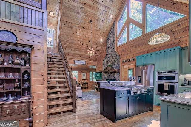 kitchen featuring light wood-type flooring, appliances with stainless steel finishes, decorative light fixtures, high vaulted ceiling, and wooden walls