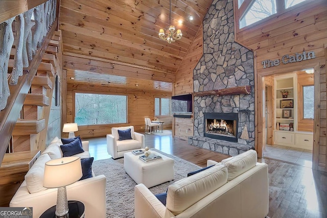 living room featuring built in features, wood finished floors, an inviting chandelier, a stone fireplace, and wood walls