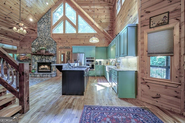 kitchen with a fireplace, stainless steel appliances, wood walls, light wood-type flooring, and green cabinetry