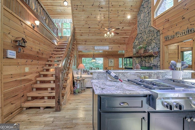 kitchen with wooden walls, light wood-style flooring, a healthy amount of sunlight, stainless steel gas stovetop, and high vaulted ceiling