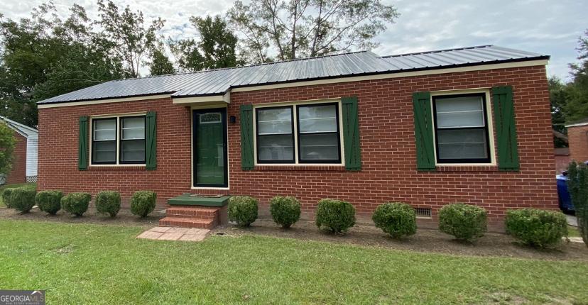 view of front of property featuring a front lawn, metal roof, and brick siding