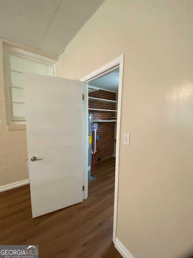 hallway with dark wood-type flooring and brick wall