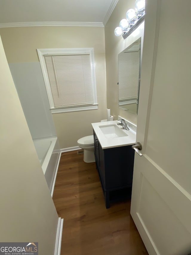 bathroom featuring vanity, crown molding, hardwood / wood-style flooring, a bath, and toilet