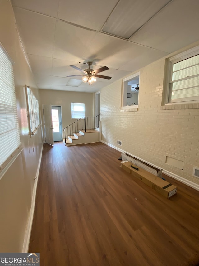 empty room with ceiling fan, dark hardwood / wood-style floors, and brick wall