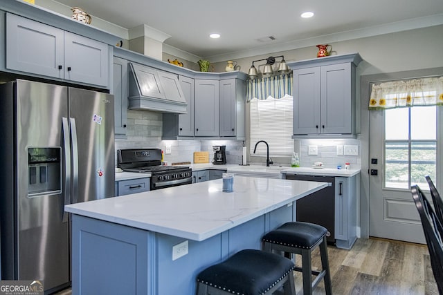 kitchen featuring light hardwood / wood-style flooring, ornamental molding, a kitchen island, custom range hood, and stainless steel appliances