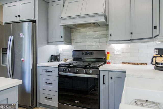 kitchen featuring backsplash, gray cabinetry, custom range hood, and appliances with stainless steel finishes