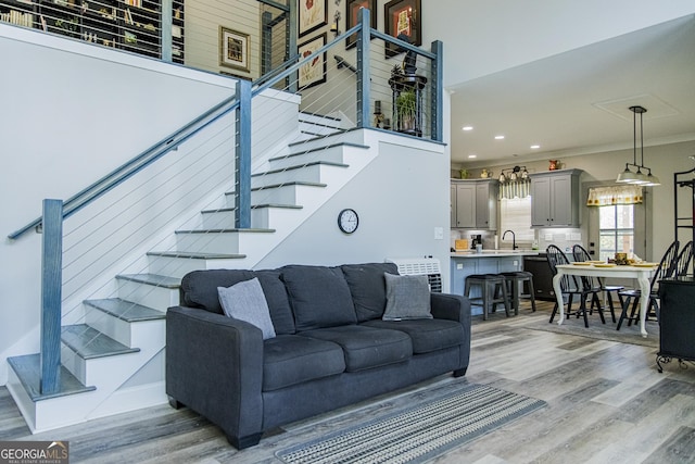 living room featuring sink, light wood-type flooring, crown molding, and a towering ceiling