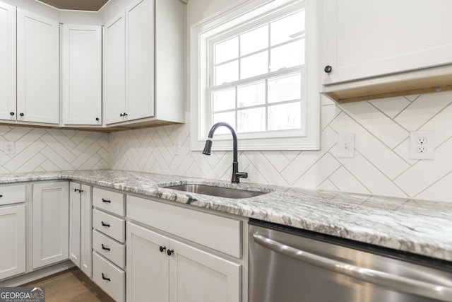 kitchen with tasteful backsplash, stainless steel dishwasher, white cabinets, a sink, and light stone countertops