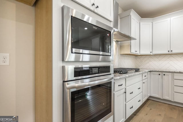 kitchen featuring wall chimney exhaust hood, appliances with stainless steel finishes, white cabinets, and tasteful backsplash