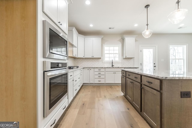 kitchen with appliances with stainless steel finishes, a sink, white cabinetry, and tasteful backsplash