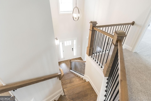 stairway with a chandelier, wood finished floors, and baseboards