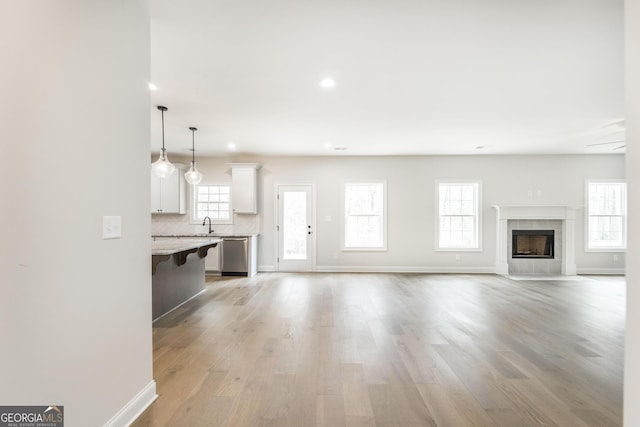 unfurnished living room featuring recessed lighting, light wood-style floors, a high end fireplace, a sink, and baseboards