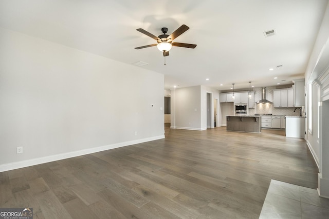 unfurnished living room with baseboards, wood finished floors, visible vents, and a ceiling fan