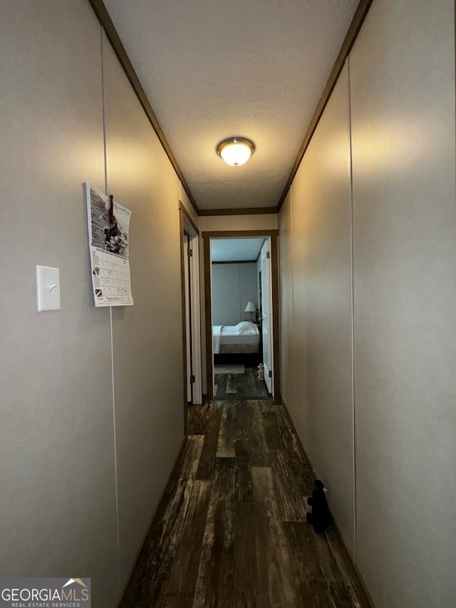 hall with a textured ceiling, dark wood-type flooring, and crown molding