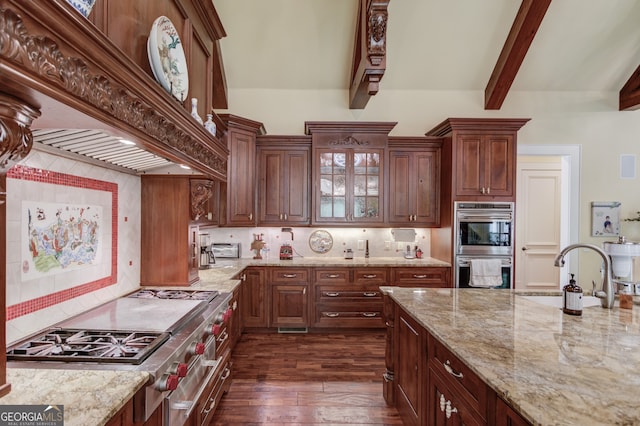 kitchen with appliances with stainless steel finishes, dark wood-type flooring, light stone counters, beamed ceiling, and custom exhaust hood