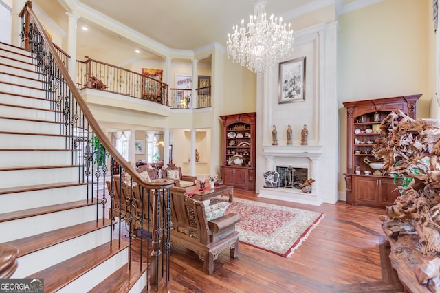 living room with a chandelier, dark wood-type flooring, ornamental molding, a high ceiling, and ornate columns