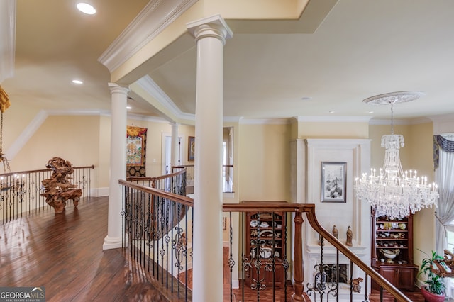 hall with dark hardwood / wood-style floors, decorative columns, ornamental molding, and an inviting chandelier