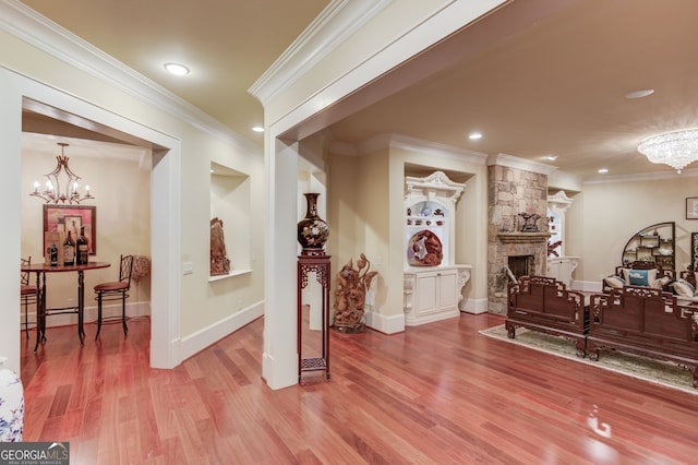 foyer entrance featuring wood-type flooring, a stone fireplace, a notable chandelier, and crown molding