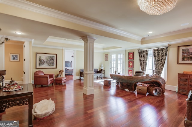 living room with ornate columns, wood-type flooring, a tray ceiling, ornamental molding, and a chandelier