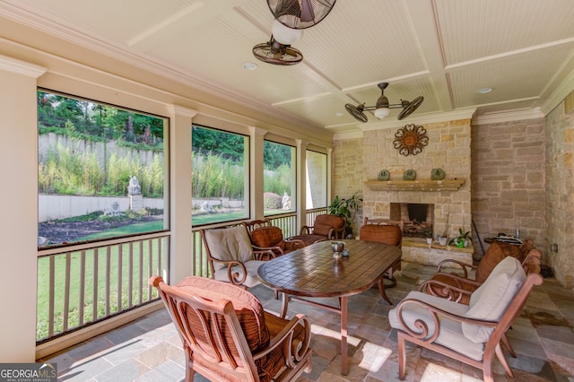 sunroom featuring a stone fireplace, coffered ceiling, ceiling fan, and beamed ceiling