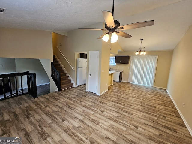 unfurnished living room with ceiling fan with notable chandelier, light wood-type flooring, and vaulted ceiling