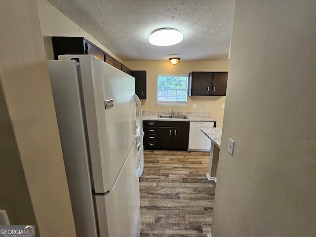 kitchen with white appliances, a textured ceiling, light hardwood / wood-style flooring, dark brown cabinetry, and sink