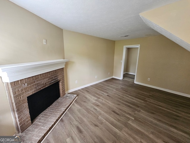 unfurnished living room featuring a brick fireplace, vaulted ceiling, a textured ceiling, and hardwood / wood-style floors