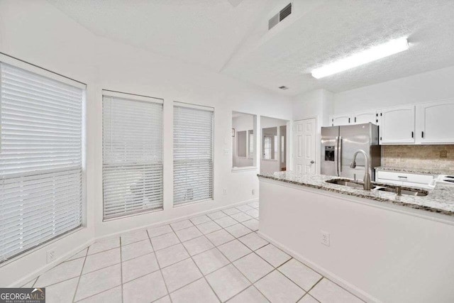 kitchen featuring light stone counters, light tile patterned flooring, sink, stainless steel fridge with ice dispenser, and white cabinetry