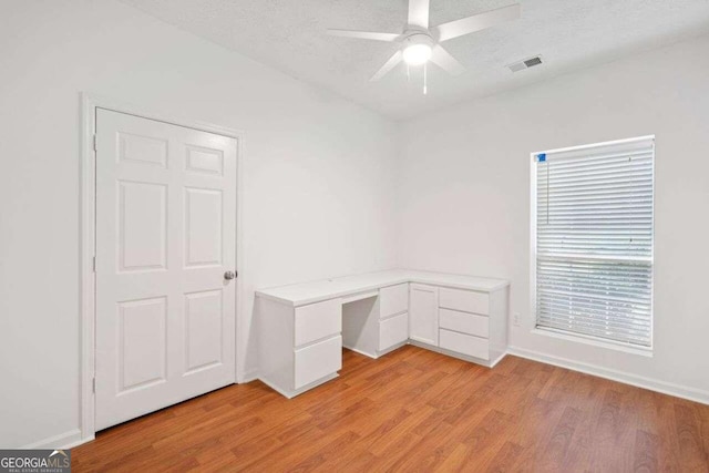 unfurnished office with ceiling fan, a textured ceiling, built in desk, and light hardwood / wood-style floors