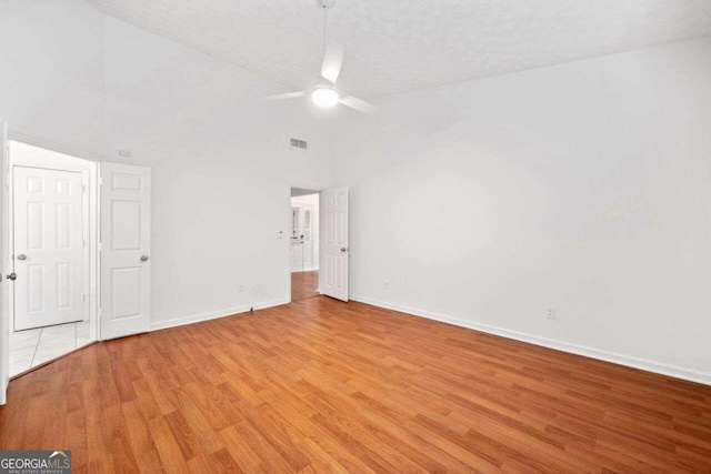 unfurnished room featuring light wood-type flooring, vaulted ceiling, ceiling fan, and a textured ceiling