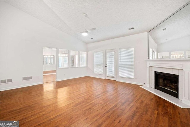 unfurnished living room featuring high vaulted ceiling, a tile fireplace, a textured ceiling, ceiling fan, and hardwood / wood-style flooring