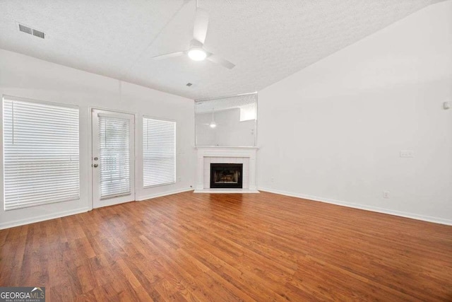 unfurnished living room with a fireplace, a textured ceiling, lofted ceiling, ceiling fan, and hardwood / wood-style floors