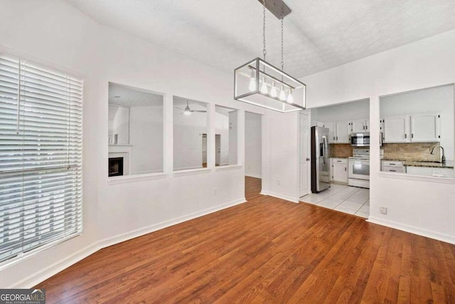 unfurnished dining area featuring a textured ceiling, ceiling fan with notable chandelier, vaulted ceiling, and light hardwood / wood-style flooring