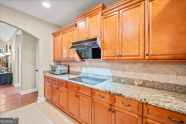 kitchen with black electric stovetop, light hardwood / wood-style floors, light stone countertops, and backsplash