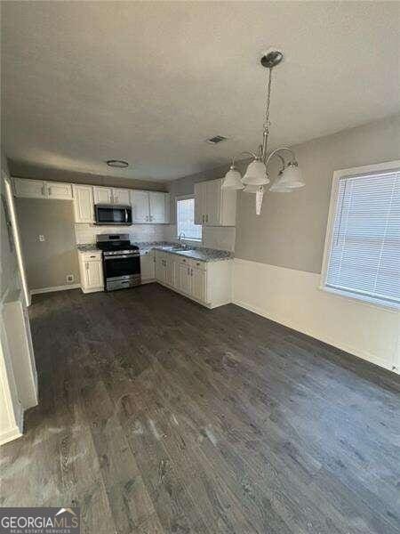 kitchen featuring dark hardwood / wood-style floors, a notable chandelier, white cabinetry, stainless steel appliances, and decorative light fixtures