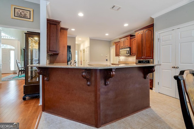 kitchen featuring a kitchen bar, kitchen peninsula, crown molding, sink, and light tile patterned floors