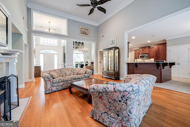 living room featuring a towering ceiling, light hardwood / wood-style floors, ceiling fan with notable chandelier, and ornamental molding