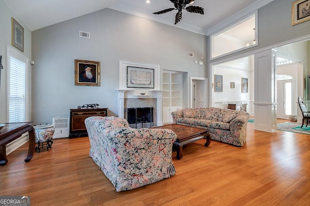 living room featuring ceiling fan, built in shelves, a towering ceiling, light hardwood / wood-style floors, and decorative columns