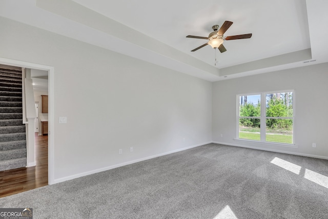 carpeted spare room featuring a tray ceiling and ceiling fan