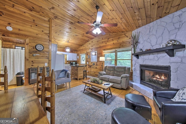 living area featuring lofted ceiling, light wood-style floors, wood walls, a stone fireplace, and wooden ceiling